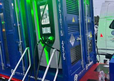 Mobiler Energiecontainer von FleetBoost mit integrierter Ladeeinheit und grüner Statusbeleuchtung, aufgestellt auf einem Trailer mit Zugangstreppe auf einem Betriebsgelände.