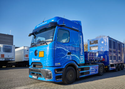 Elektrisch betriebener Lkw von FleetBoost mit angekoppeltem mobilem Energiecontainer steht auf einem Logistikgelände, bereitgestellt für flexible Stromversorgung und Ladeinfrastruktur.